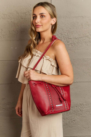 Woman with Nicole Lee USA Amy Studded Bucket Bag in red vegan leather, showing stud and zipper detailing on the front.