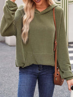 Woman wearing textured kangaroo pocket long sleeve hoodie in green, paired with blue jeans and a brown crossbody bag