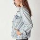 Woman wearing a distressed button-up denim jacket by Risen Jeans, showcasing frayed details and a rugged, edgy style.