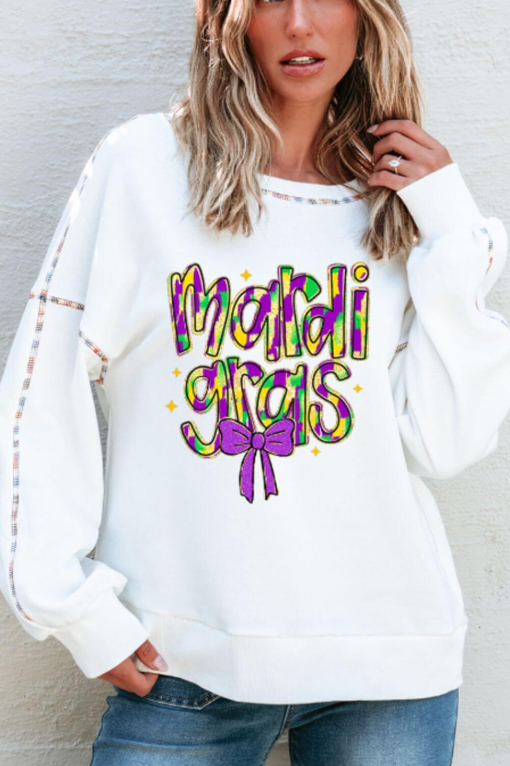 Bella Road MARDI GRAS white sweatshirt featuring colorful text and a bow, perfect for festive celebrations.