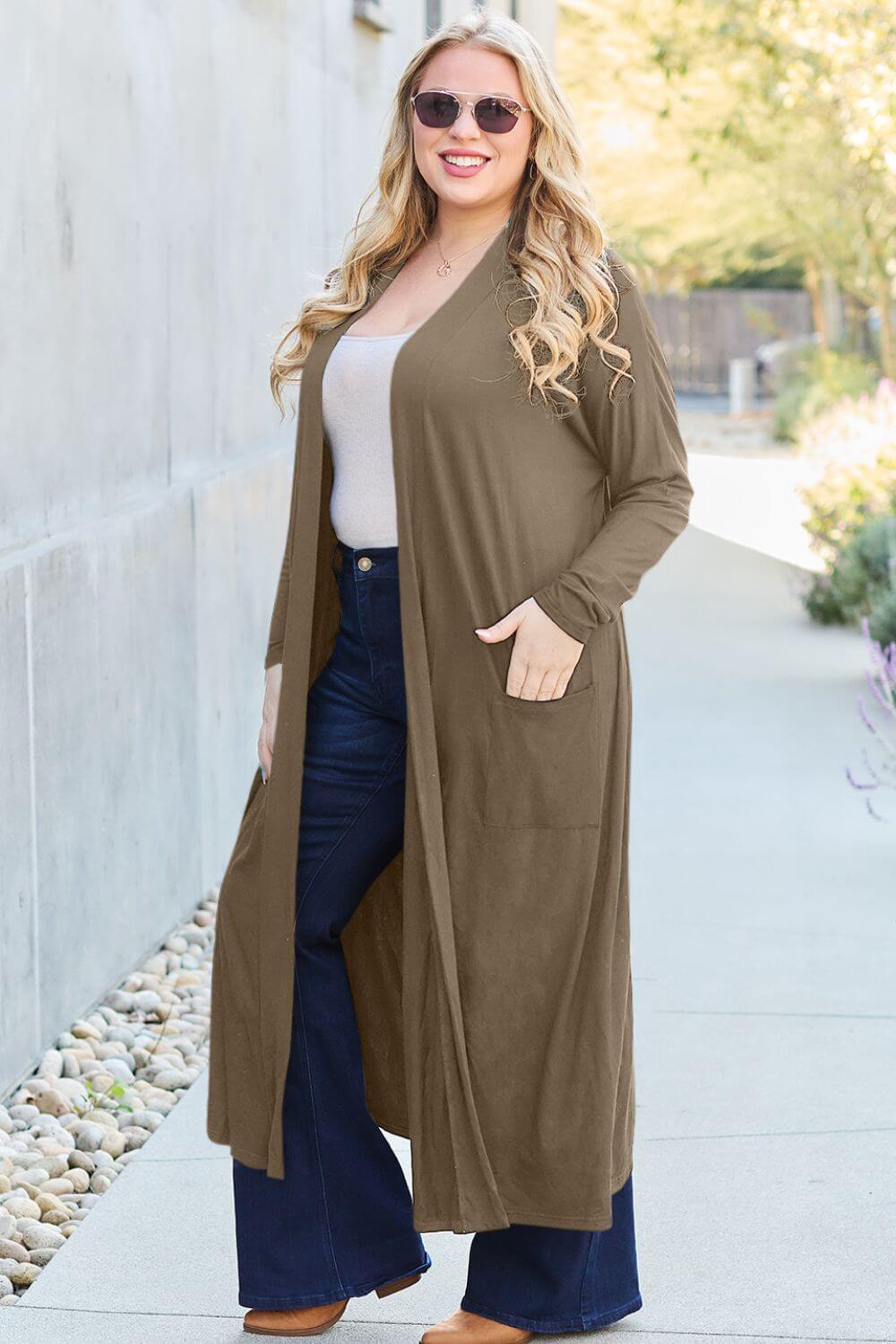 Woman wearing open front long sleeve cover up with pockets, styled with sunglasses, jeans, and white top, walking outdoors.