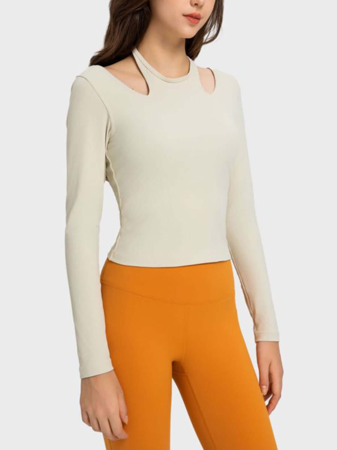 Model showcasing the Millennia Halter Neck Long Sleeve Sporty Top in cream with stylish cutouts and orange leggings.