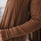 Woman wearing a textured brown open front cover up with pockets over a white shirt.