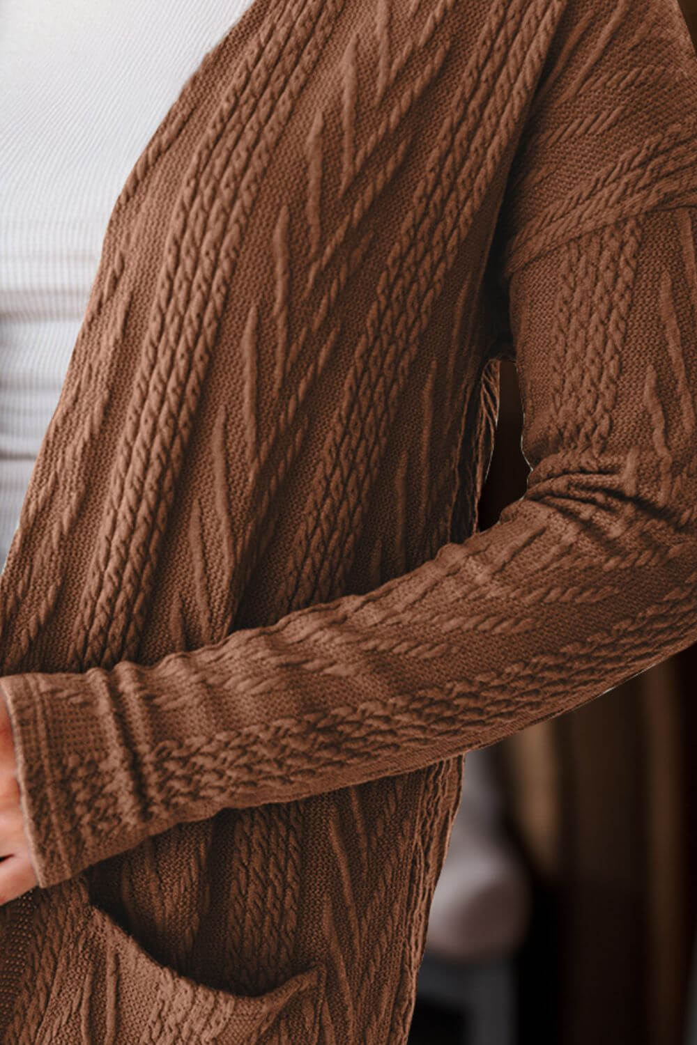 Woman wearing a textured brown open front cover up with pockets over a white shirt.