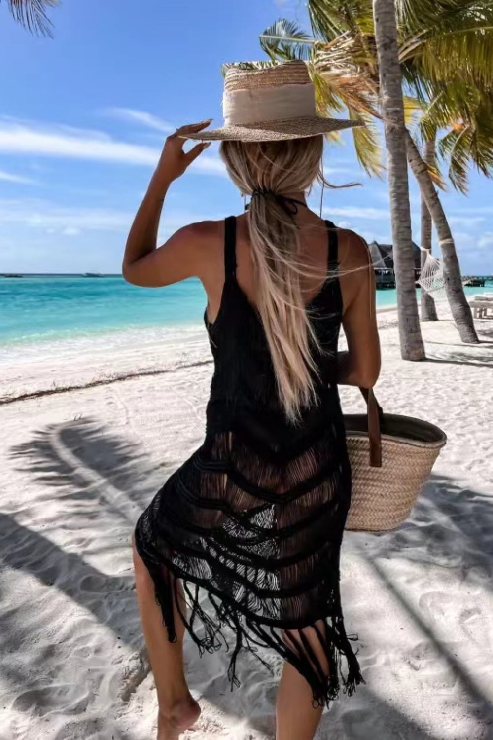 Woman in a black fringe cover-up and straw hat enjoying a beach view, perfect for a stylish poolside look.