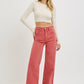 Woman wearing full size high rise tummy control wide leg jeans in rose color paired with a cream top.