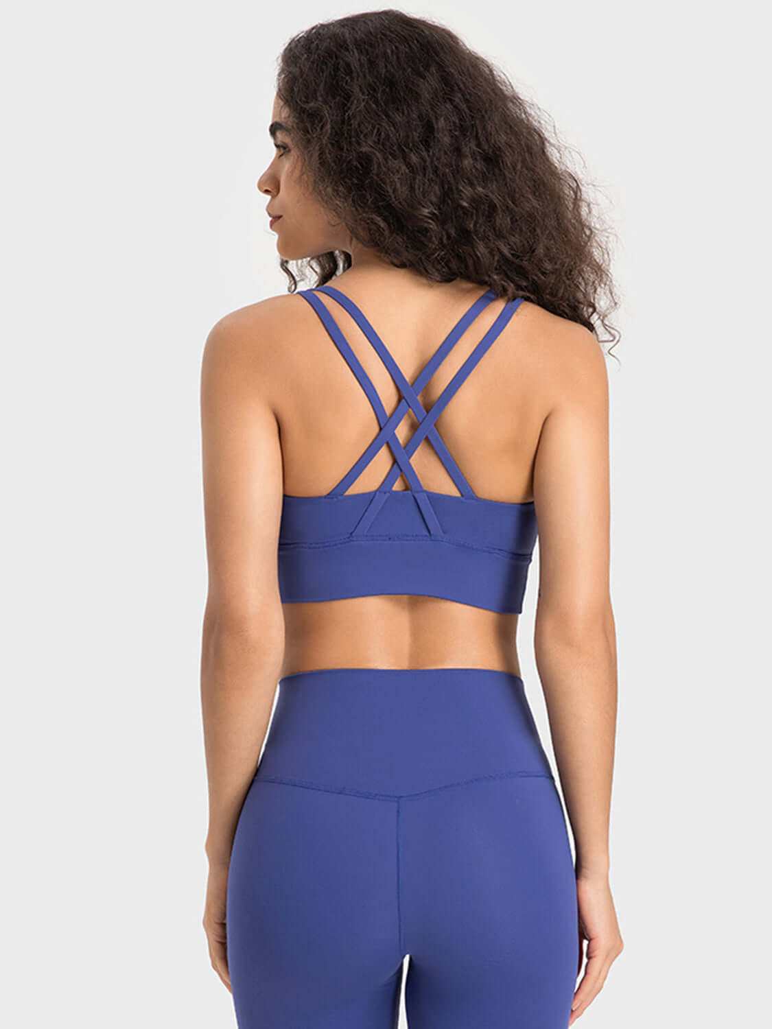 Back view of a woman in a blue crisscross active tank top, showcasing its stylish and breathable design.