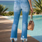 Woman wearing distressed raw hem jeans by the pool, showcasing functional pockets and a stylish, edgy look