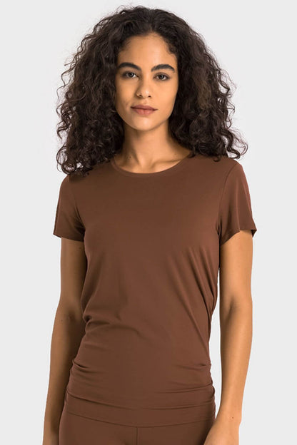 Model wearing a brown Millennia Tie Back Short Sleeve Sports Tee, showcasing the trendy design and comfortable fit for activewear.