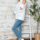 Woman wearing Bella Road Cable-Knit Cold Shoulder Sweater with jeans and sneakers, stylish and cozy fashion statement.