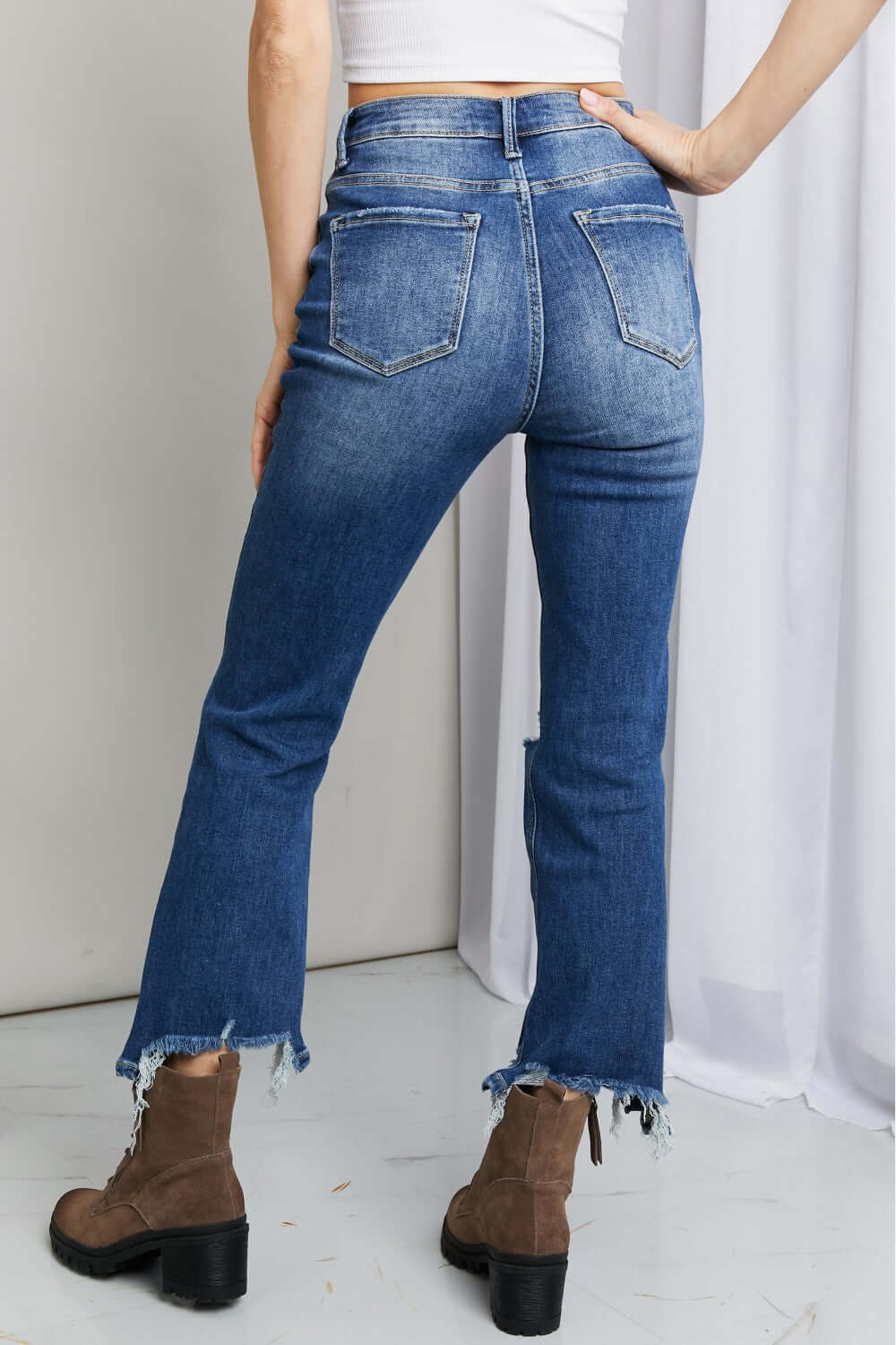 Woman wearing Frayed Hem Distressed Cropped Risen Jeans with boots, showcasing stylish raw hems and pockets for a casual look.