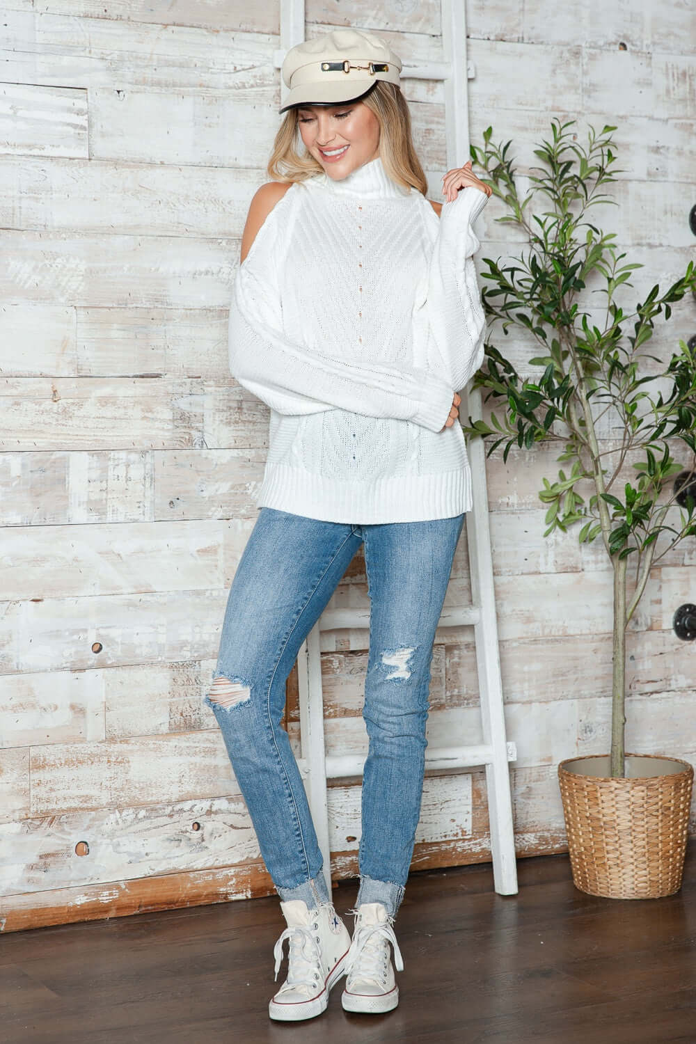 Woman wearing Bella Road Cable-Knit Cold Shoulder Turtleneck Sweater, styled with jeans and sneakers for a cozy-chic look.