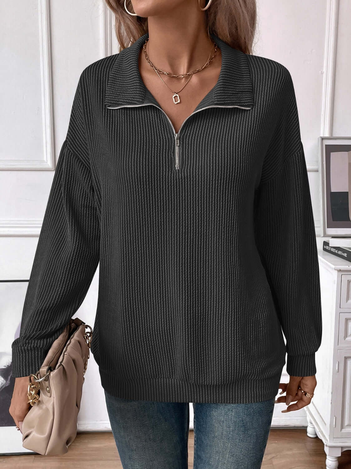 Woman wearing Striped Half Zip Long Sleeve T-Shirt in black, paired with jeans, carrying a beige handbag.