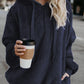 Woman in navy quarter-zip teddy hoodie holding a coffee cup on a city street. Stylish and comfortable outfit choice.