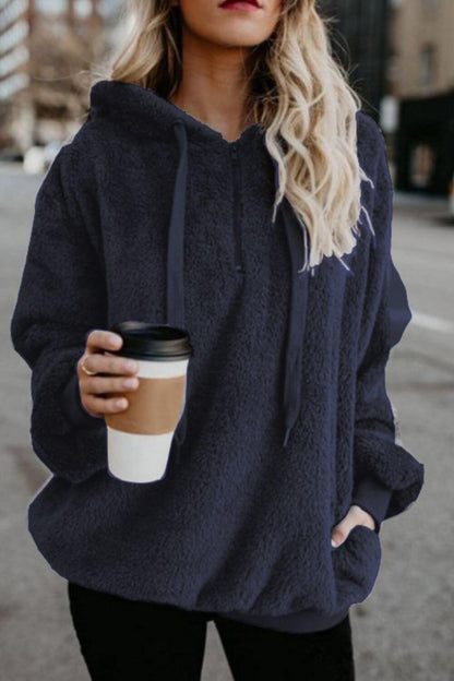 Woman in navy quarter-zip teddy hoodie holding a coffee cup on a city street. Stylish and comfortable outfit choice.