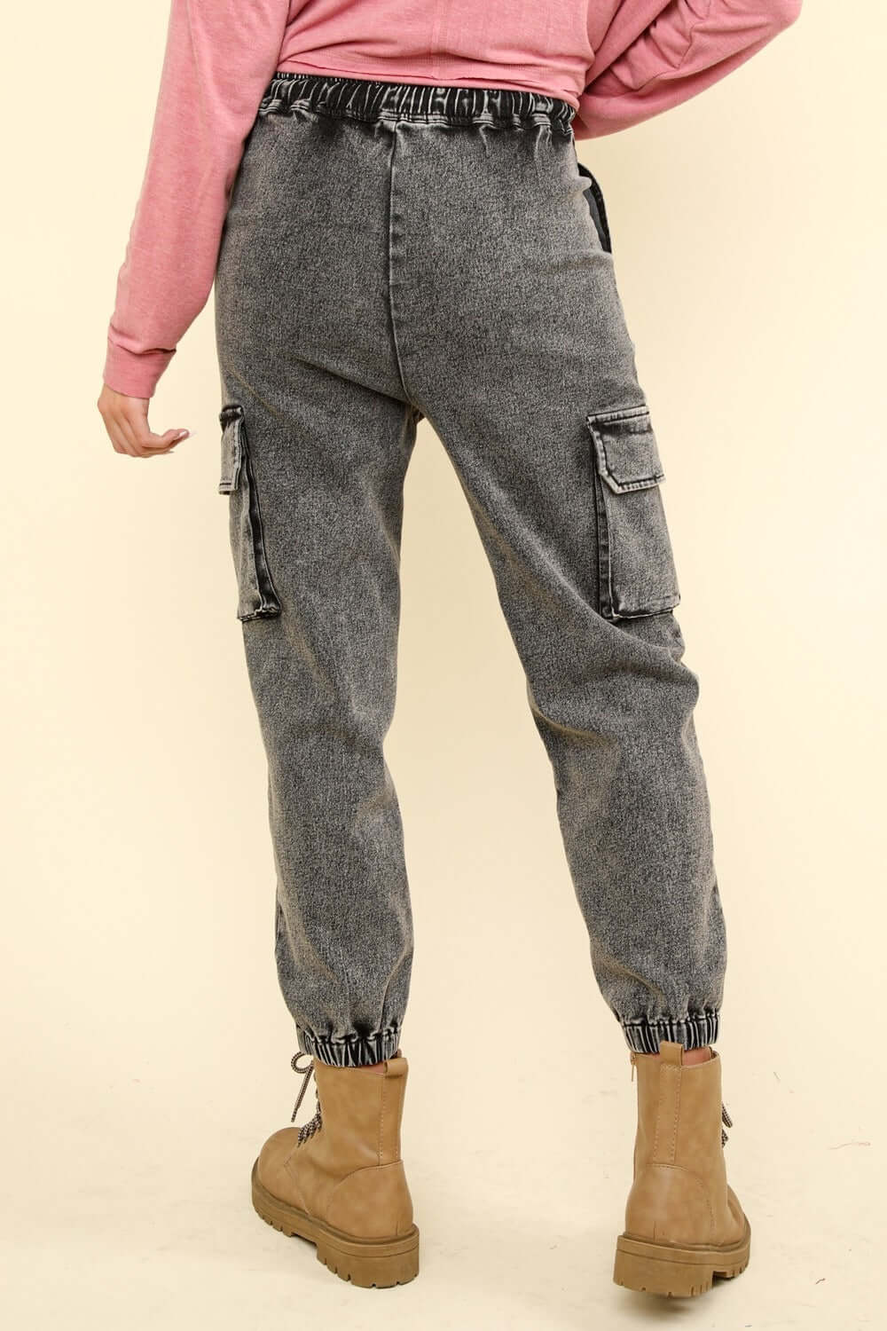 Back view of washed drawstring jogger cargo jeans with elastic waist, side pockets, and raw detail, paired with tan boots.