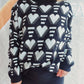 Woman wearing Bella Road Heart Contrast Long Sleeve Dropped Shoulder Sweater in black and white hearts pattern.