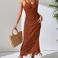 Woman wearing a rust-colored Openwork Scoop Neck Cover-Up Dress with tassel hem, holding a straw bag, and accessorized with hat and sandals.