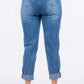 Back view of high waist pleated waist mom jeans in non-stretch denim with rolled cuffs and button closure, worn by a model with white sneakers