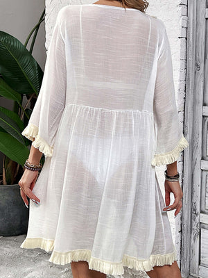 Woman wearing Fringe Tie Neck Three-Quarter Sleeve Cover Up, sheer white material with fringe details on sleeves and hem, back view.