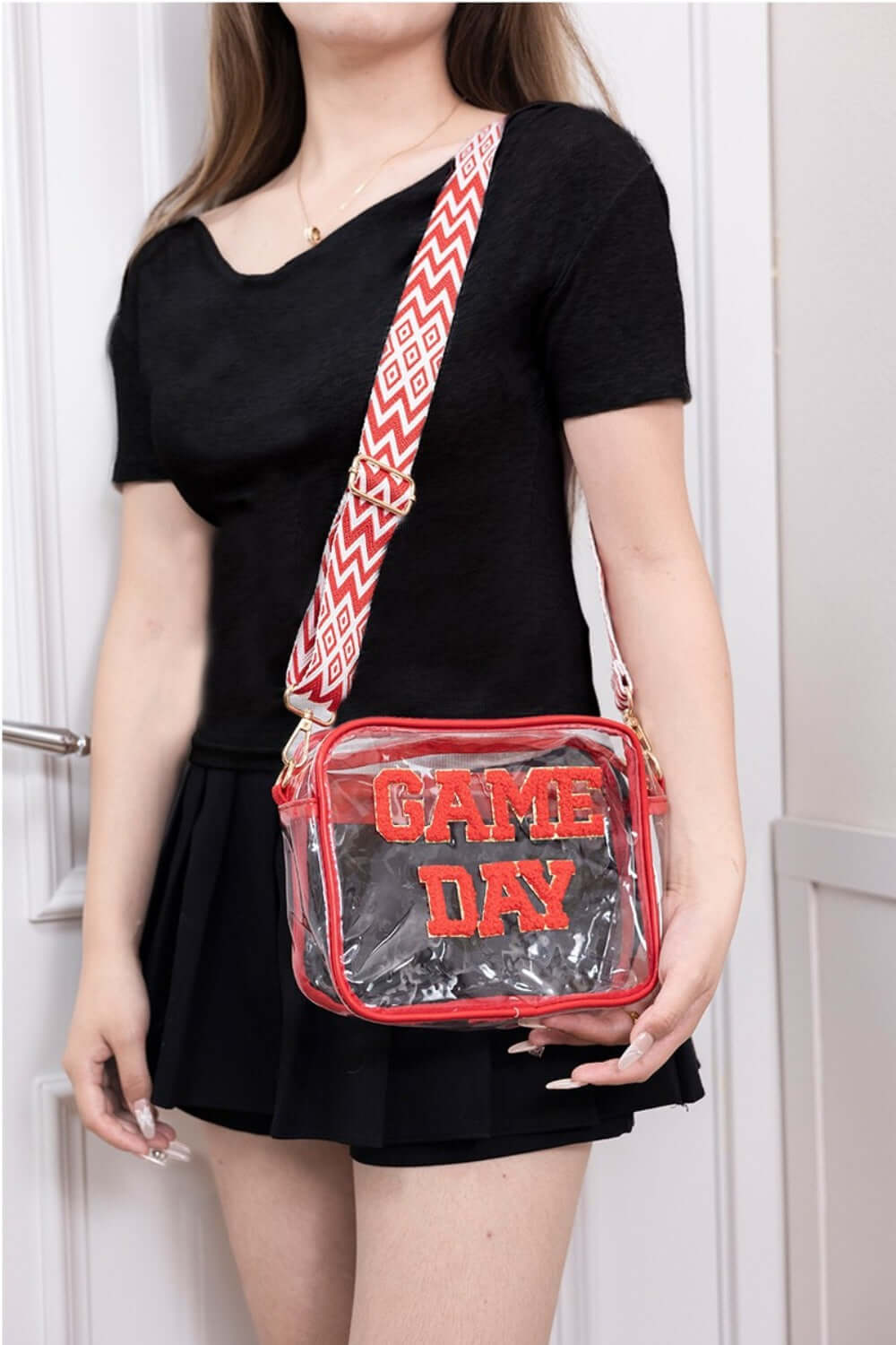 Woman holding Zenana GAME DAY transparent crossbody bag with red glitter trim and adjustable strap.