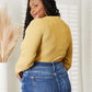 Woman wearing All About Details Full Size Ribbed Bodysuit in mustard yellow, paired with high-waisted blue jeans, showing back view.