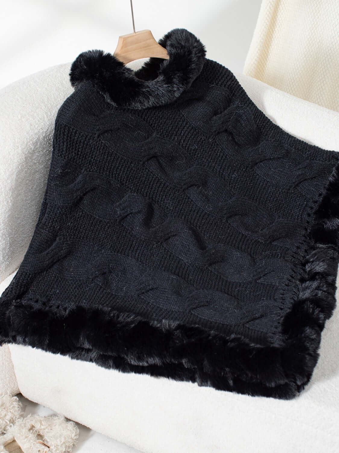 Bella Road black fuzzy hem cable-knit poncho draped on a chair, perfect for chilly days in stylish warmth.