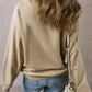 Woman wearing a Bella Road Thankful Round Neck Long Sleeve Sweatshirt in beige with blue jeans, showing back view holding a white handbag