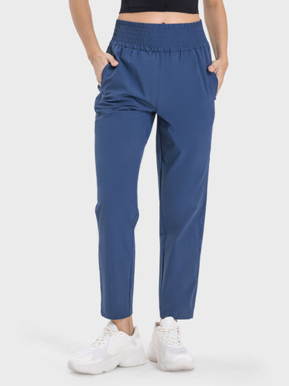 Woman in blue Millennia Pocketed High Waist Active Pants, featuring elastic waistband and side pockets for comfort and style.