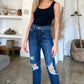 Woman wearing High Waist Rigid Magic Heavy Destroy Straight Judy Blue Jeans with heavy distressing and black tank top in a stylish room.