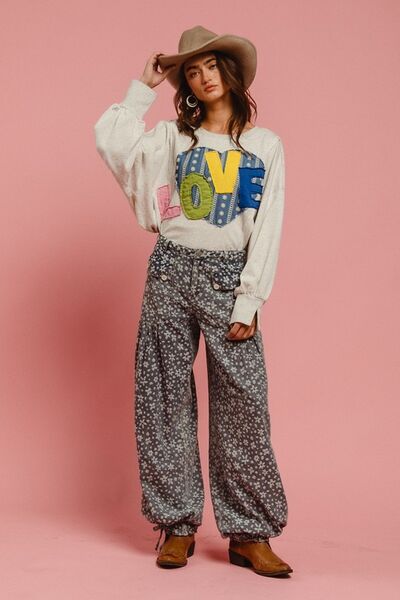 Model wearing LOVE graphic sweatshirt and floral pants against a pink background, showcasing casual and stylish vibes.