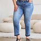 Woman wearing Judy Blue release hem cropped bootcut jeans with a white top and black sandals in a stylish indoor setting