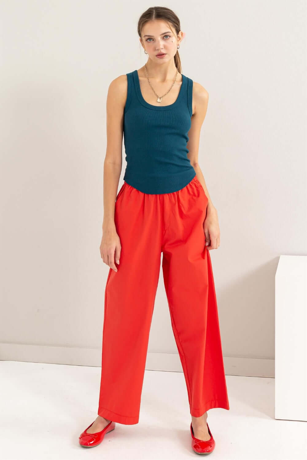 Woman wearing Ribbed Scoop Neck Racerback Tank in teal with red wide-leg pants and red flats, standing against a neutral background.