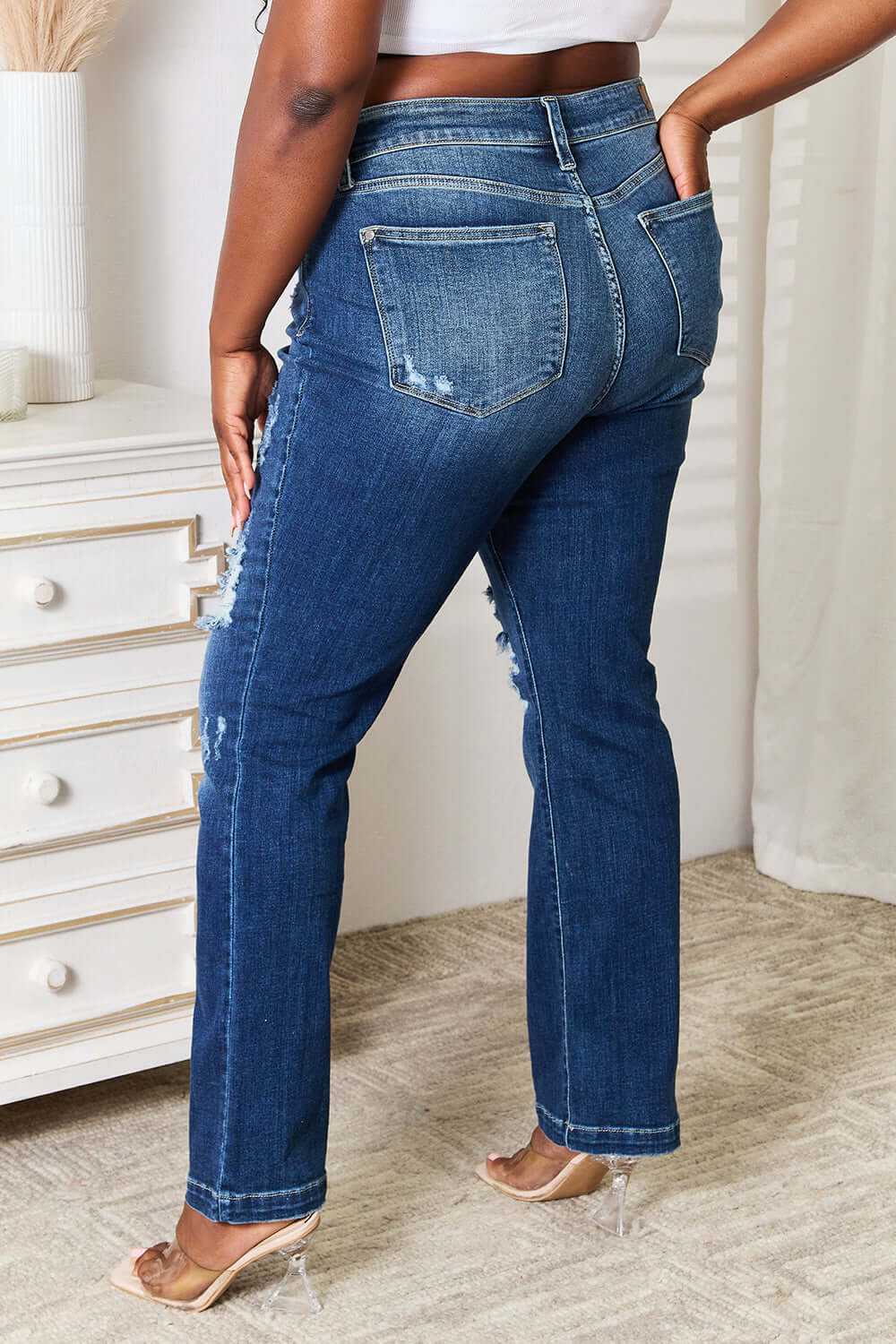 Back view of model wearing Judy Blue Mid Rise Hand Sand & Destroy Bootcut Jeans Petite in a distressed style and slightly stretchy material