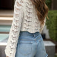 Woman wearing a cream openwork flare sleeve cover-up with denim shorts, showcasing a stylish summer look.