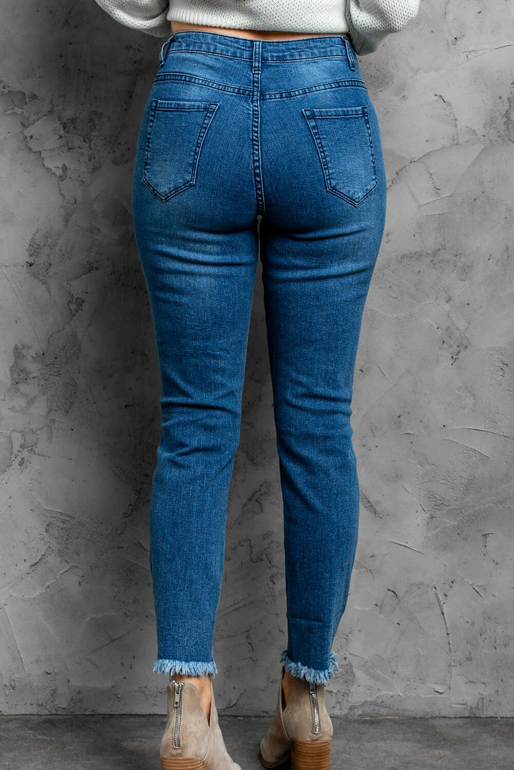 Back view of stylish distressed cropped jeans with frayed hems in blue denim, showcasing casual design and slight stretch fabric.