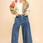 Woman in colorful sweater and wide leg mid-rise jeans, showcasing a trendy, relaxed style with drawstring hem.