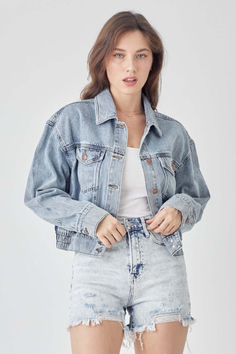 Woman wearing RISEN full size button down cropped denim jacket with distressed shorts, showcasing trendy and fashionable outerwear piece.