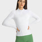 Model showing the Millennia Half Zip Thumbhole Sleeve Sports Top in white, paired with green leggings for a stylish workout look.