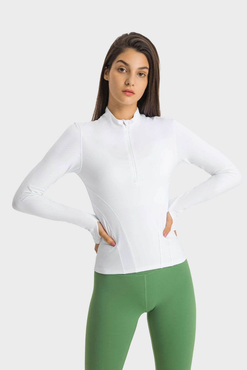 Model showing the Millennia Half Zip Thumbhole Sleeve Sports Top in white, paired with green leggings for a stylish workout look.