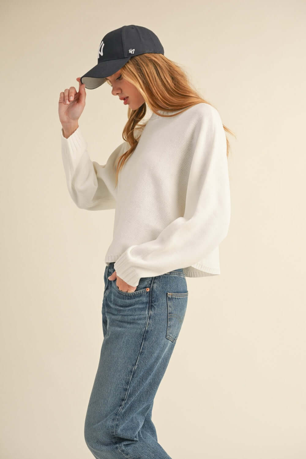 Woman wearing Bella Road Mable Round Neck Dolman Sleeve Cropped Sweater with jeans and a baseball cap.