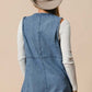 Back view of BiBi Braided Trim Open Front Denim Vest with Pockets, styled with a hat and layered over a long-sleeve top.