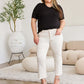 Woman wearing high waist raw hem jeans and black top posing stylishly in a chic, modern living room.