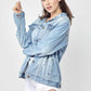 Woman modeling Distressed Long Sleeve Denim Jacket by Risen Jeans, adding a touch of edgy vintage style to her casual outfit.