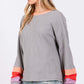 Woman wearing a gray color block waffle knit t-shirt with colorful raglan sleeves and a contrast crew neckline, paired with light jeans.