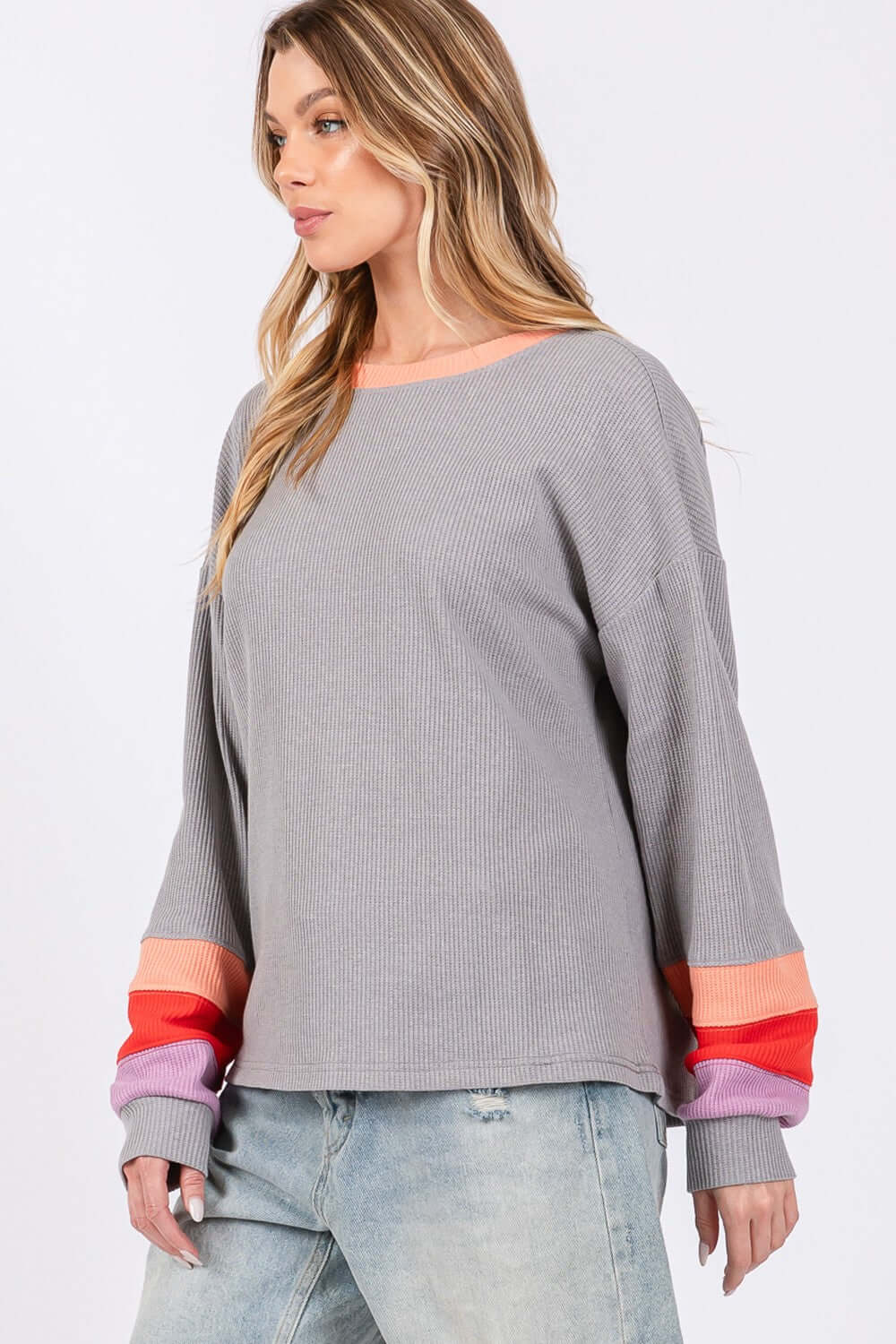 Woman wearing a gray color block waffle knit t-shirt with colorful raglan sleeves and a contrast crew neckline, paired with light jeans.