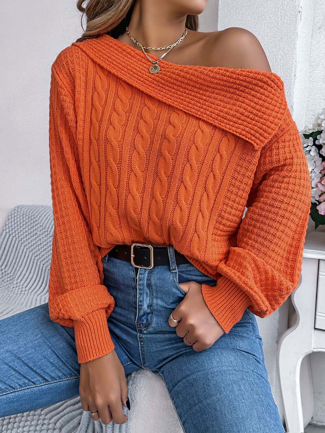 Woman wearing the Bella Road Cable-Knit One Shoulder Long Sleeve Sweater in orange, paired with high-waisted jeans, showcasing the trendy one-shoulder design