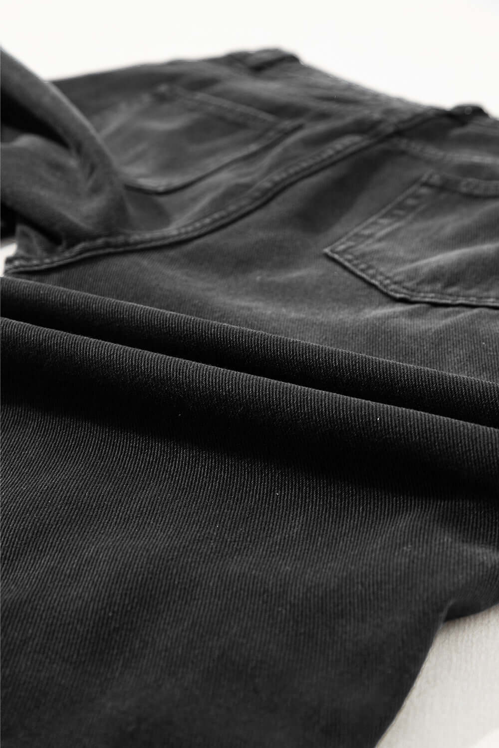 Black distressed raw hem jeans with pockets and no stretch, made from 100% cotton and seen close-up.