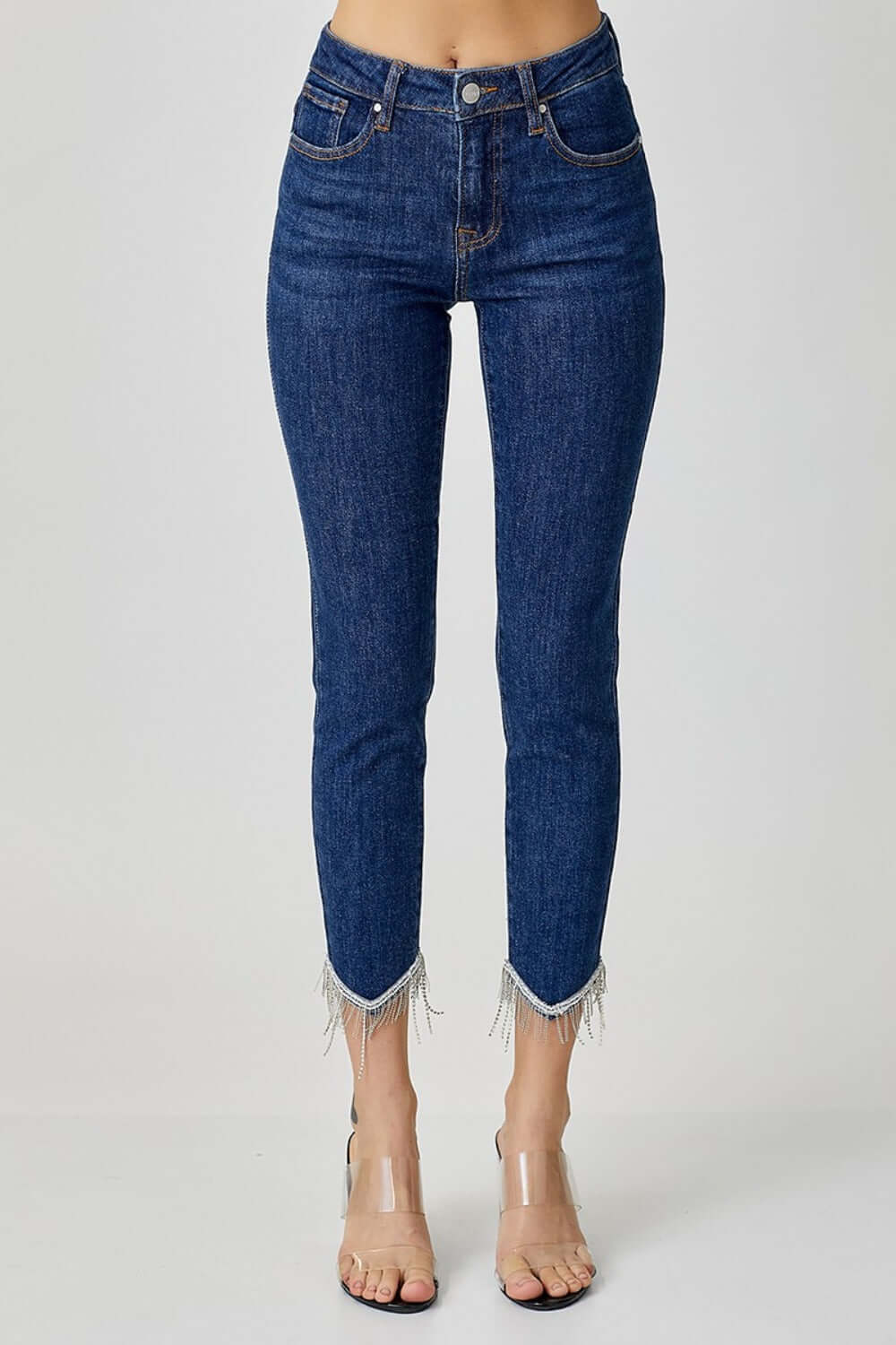 Embellished mid-rise crop skinny jeans with fringe detail, shown on model with clear heels. Fashionable and versatile denim.