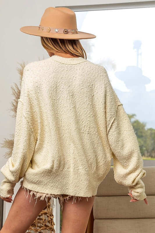 Stylish woman in a cozy cream cardigan and wide-brimmed hat, showcasing a relaxed look against a bright backdrop.